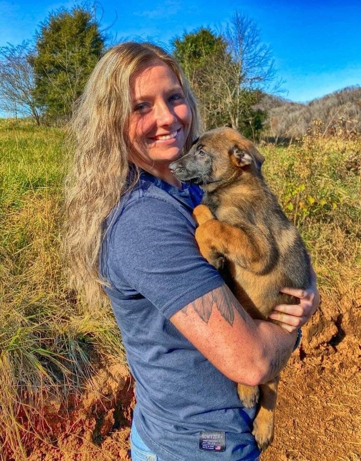 New owner holding a Belgian Malinois puppy outdoors